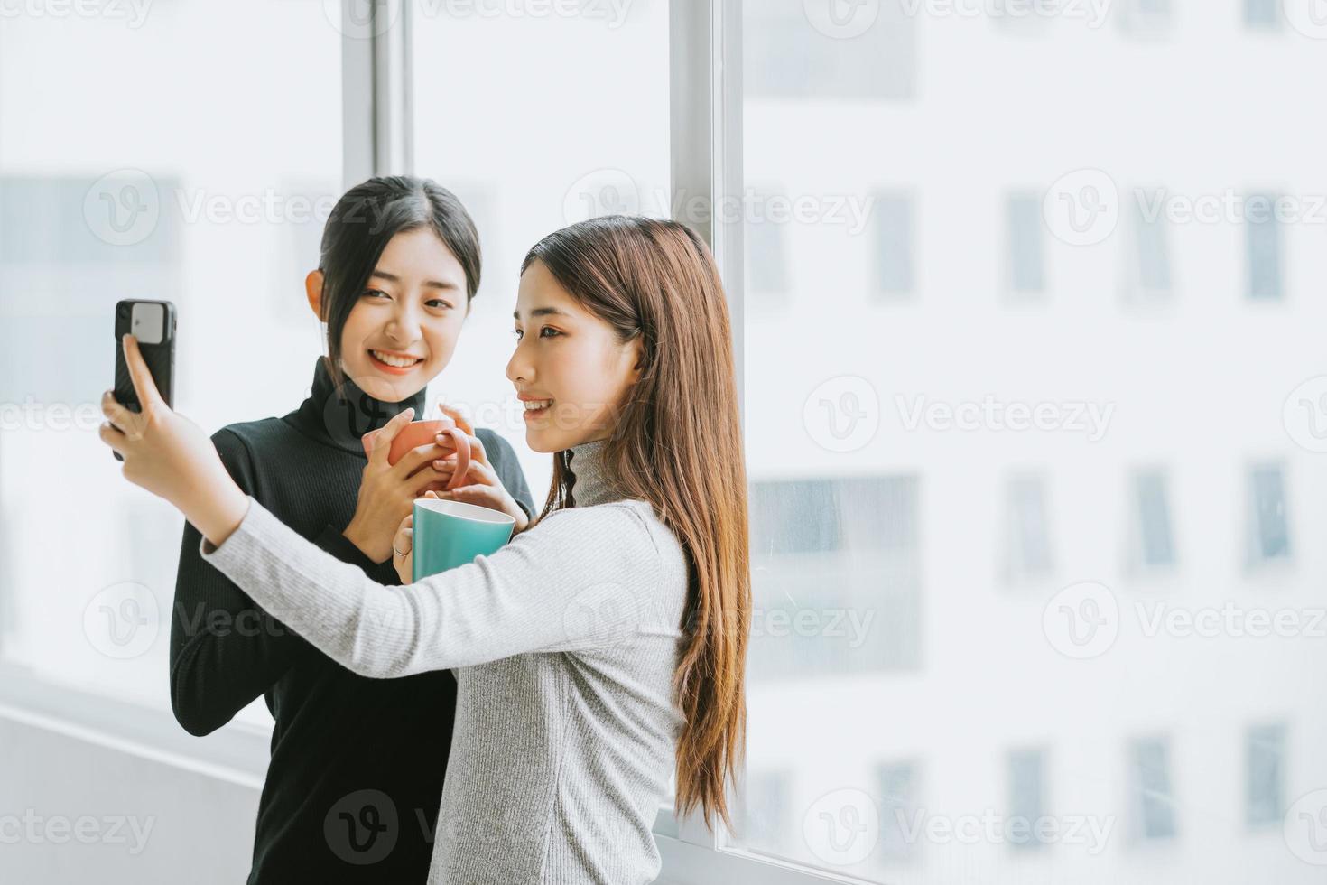 duas mulheres de negócios asiáticas conversavam perto da janela durante o recreio foto