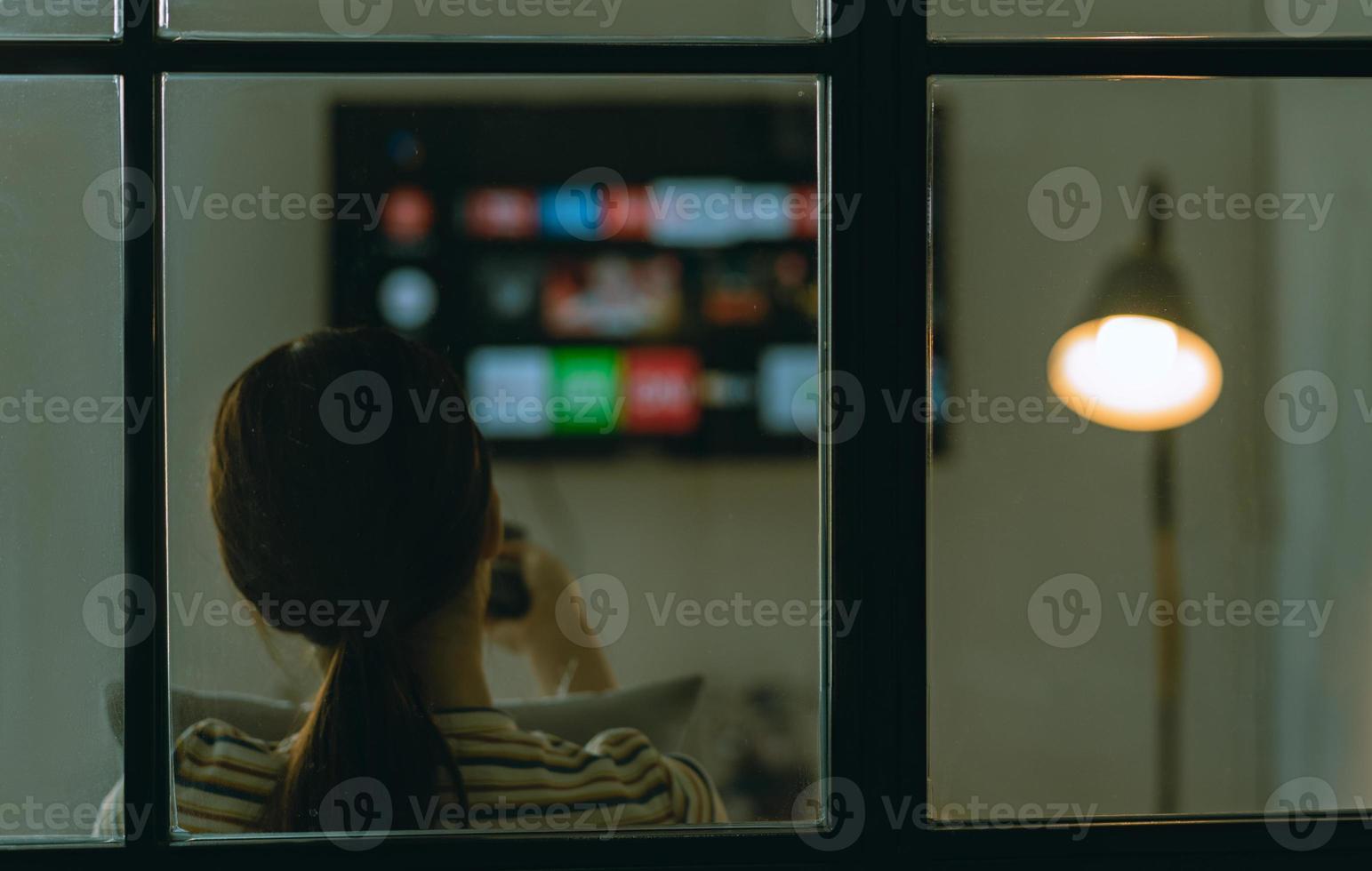 imagem borrada de mulher asiática sentada assistindo televisão sozinha no sofá à noite foto