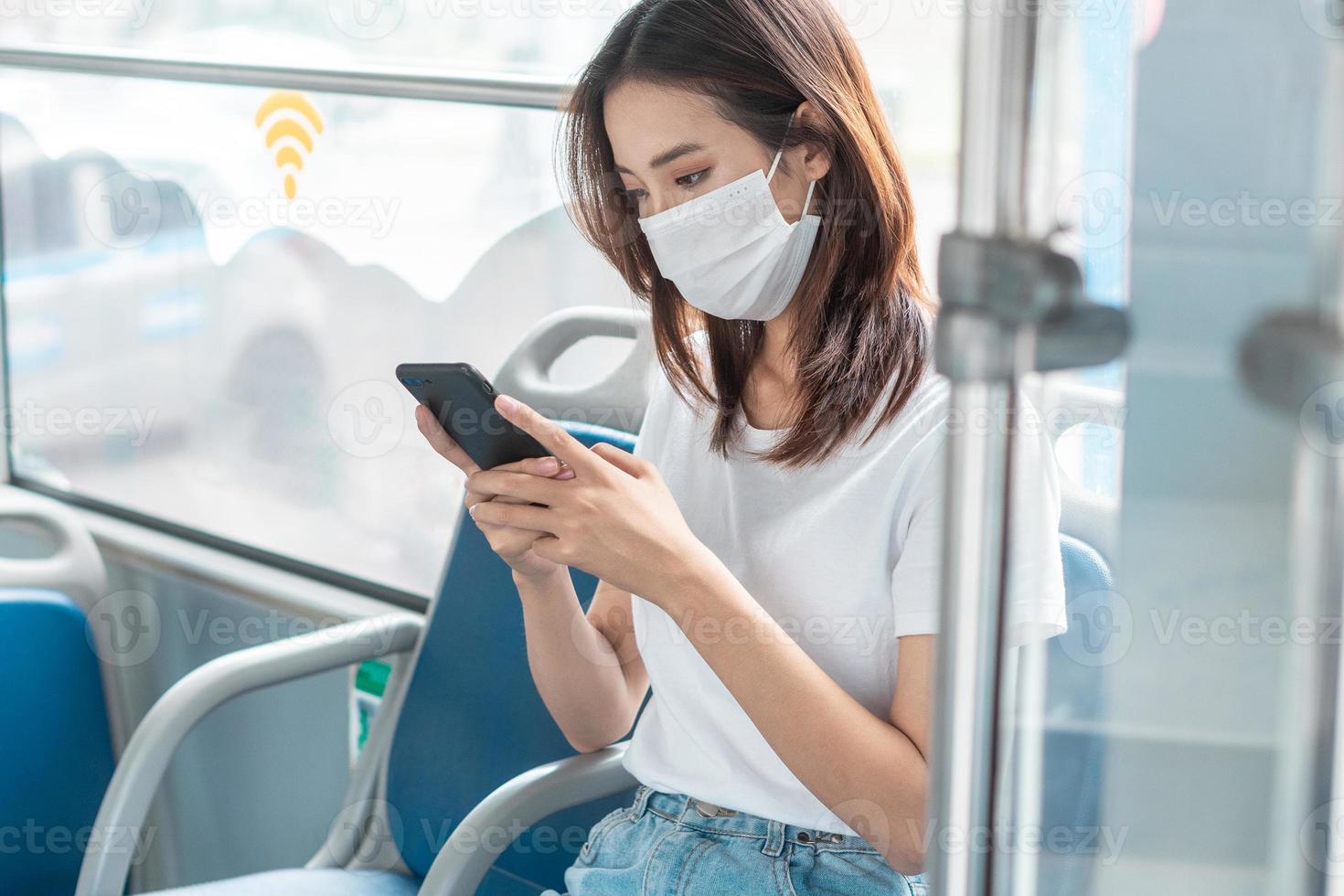 menina asiática usando máscara enquanto usa smartphone no ônibus foto