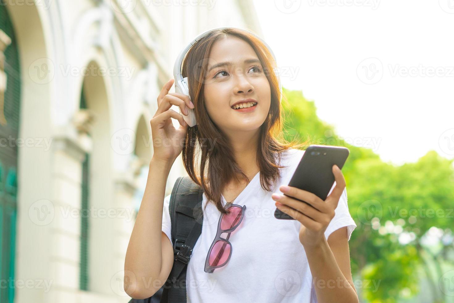 jovem asiática lendo texto em seu telefone e usando fones de ouvido para ouvir música na rua foto