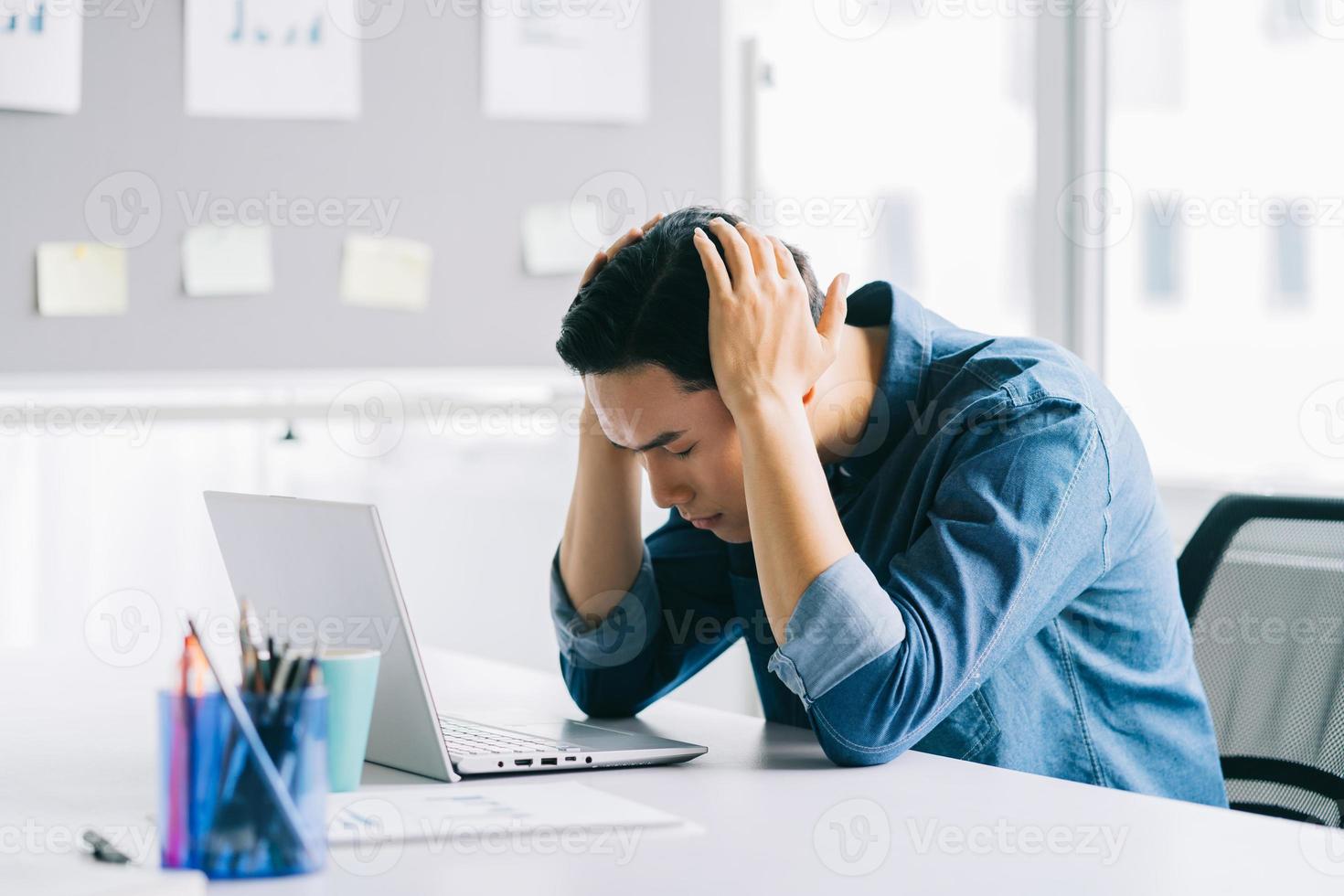 o homem asiático está segurando a cabeça dele cansado de ter que trabalhar muito foto