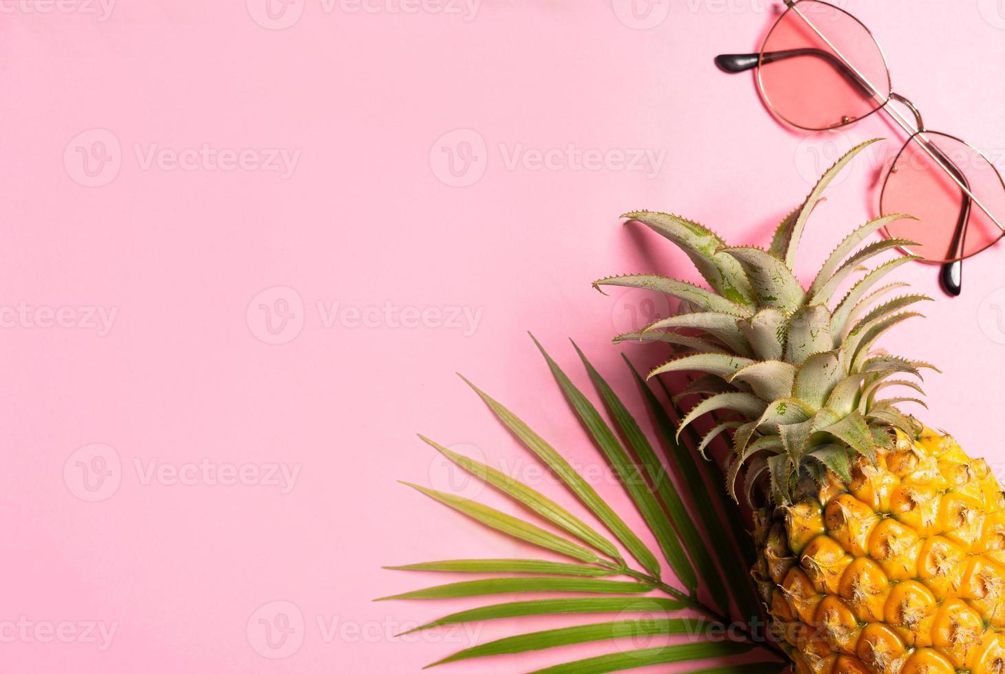 conceito de verão com abacaxi, óculos escuros e folha de palmeira em fundo rosa foto