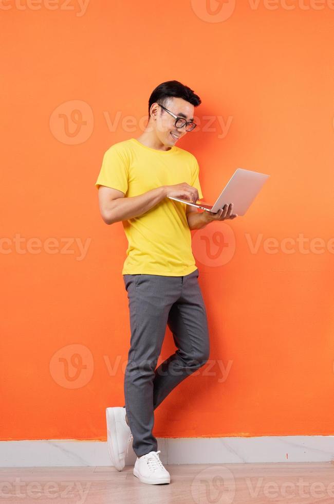 foto de corpo inteiro de homem asiático em camisa amarela em fundo laranja