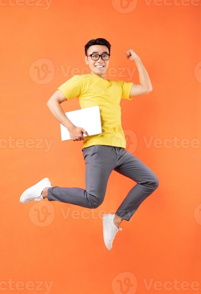 homem asiático com camiseta amarela pulando no fundo laranja foto