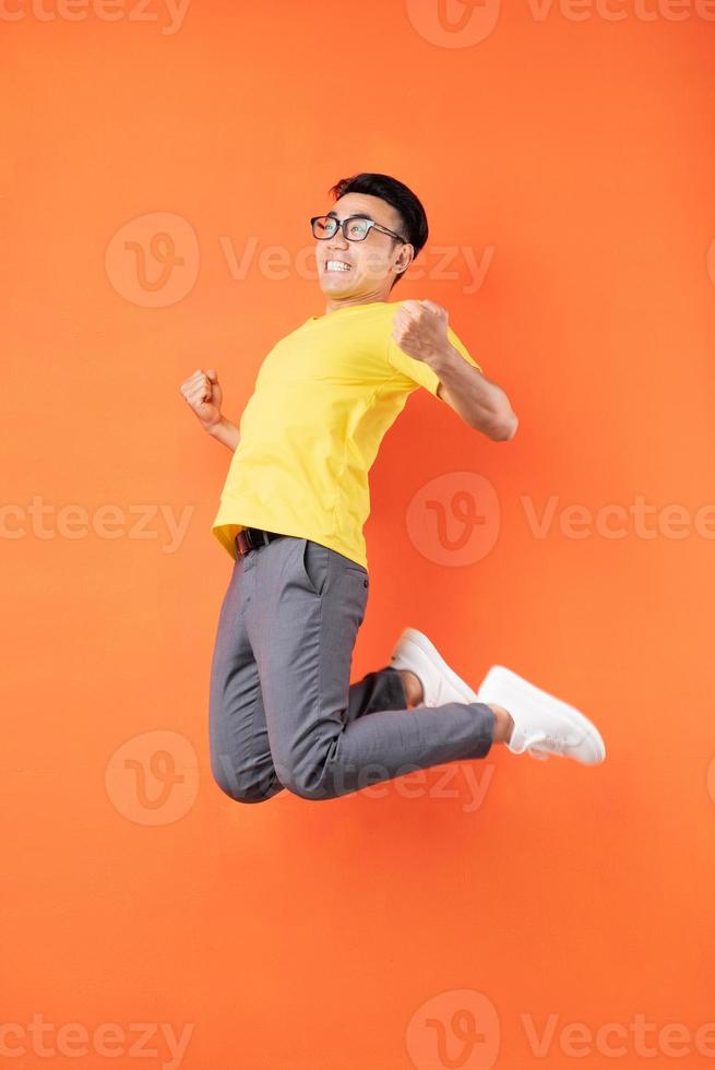 homem asiático com camiseta amarela pulando no fundo laranja foto