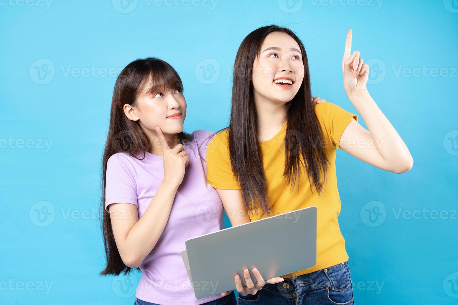 duas lindas garotas asiáticas usando laptop sobre fundo azul foto