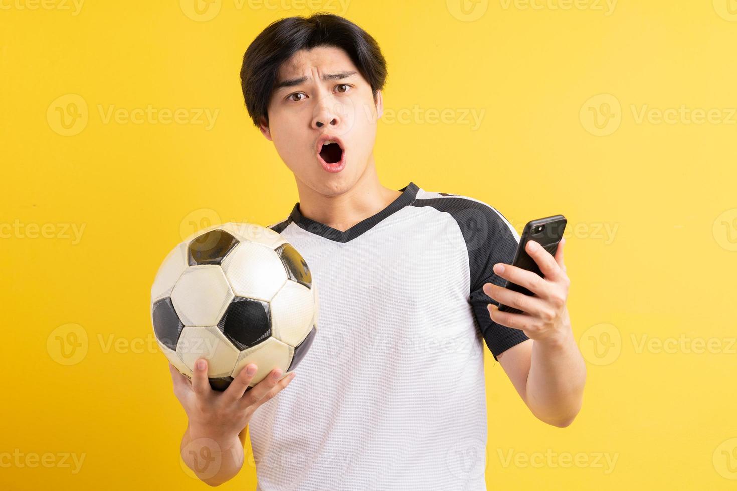 homem asiático está segurando uma bola e segurando um telefone na mão foto