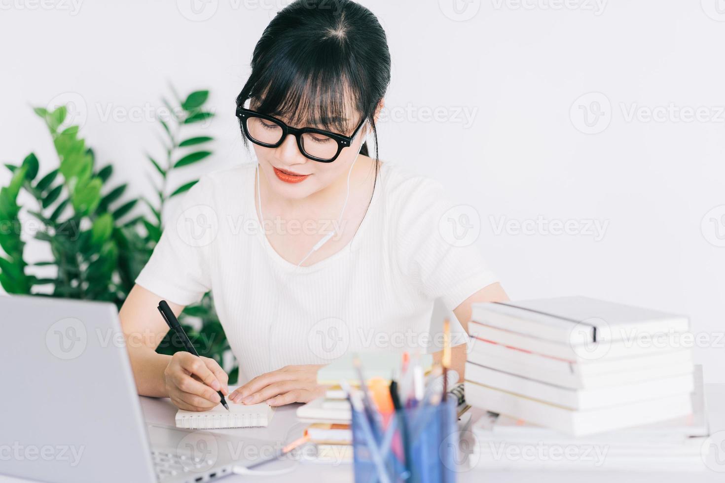 menina asiática está fazendo anotações e estudando online no laptop foto