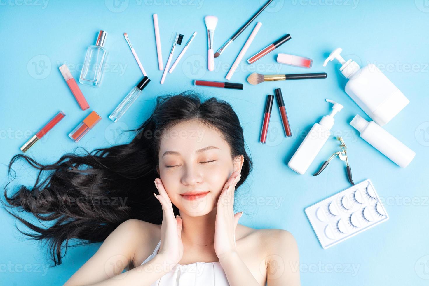 mulher asiática deitada sobre um fundo azul com maquiagem ao redor foto