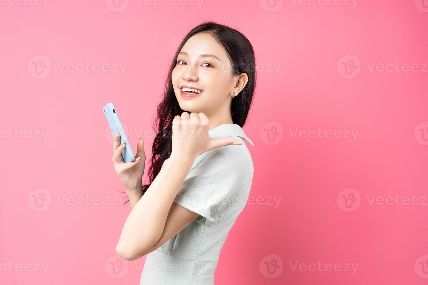 jovem mulher asiática segurando o telefone na mão e apontando para trás foto