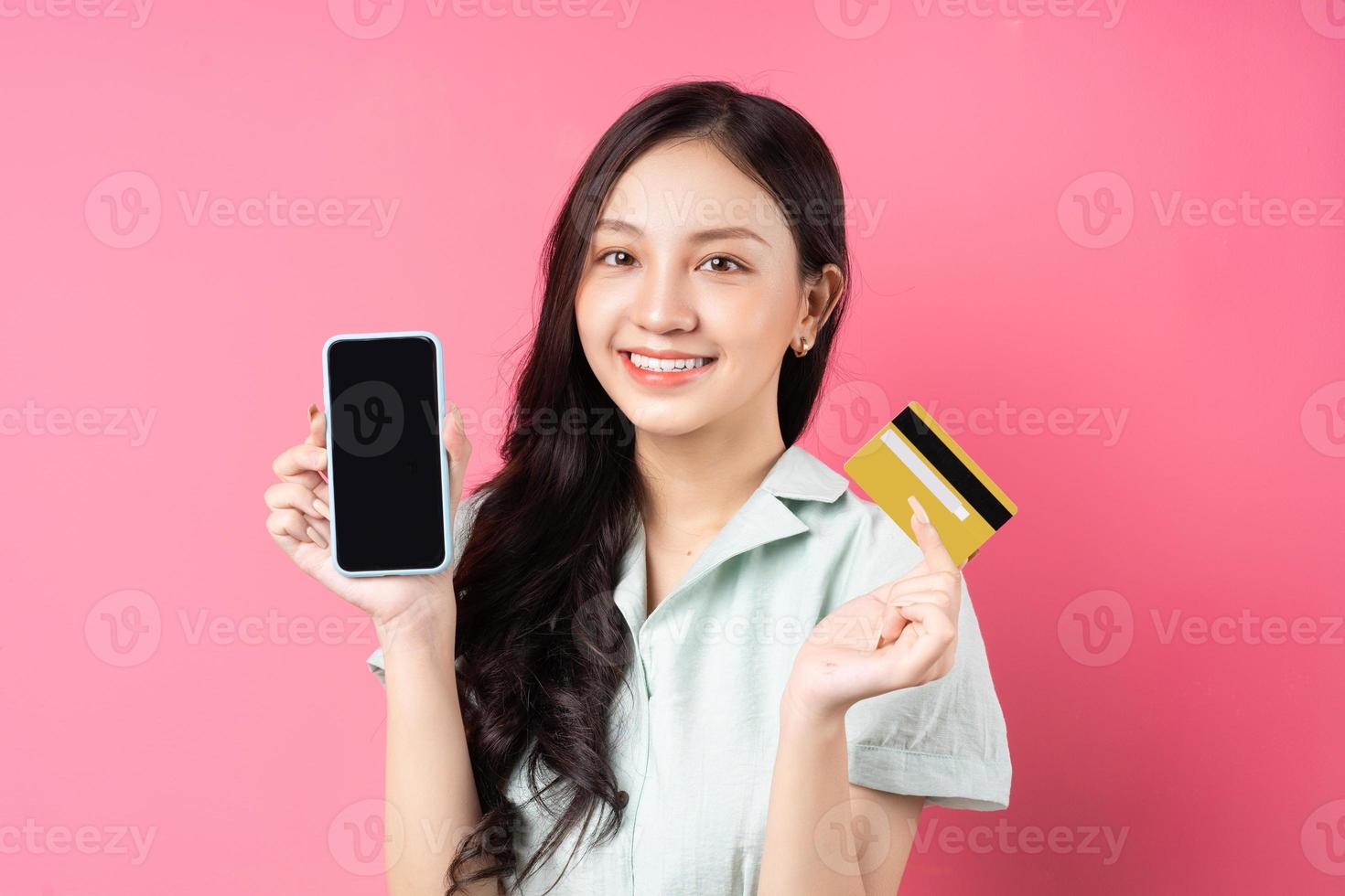 jovem mulher asiática segurando um telefone celular enquanto segura um cartão do banco na mão foto