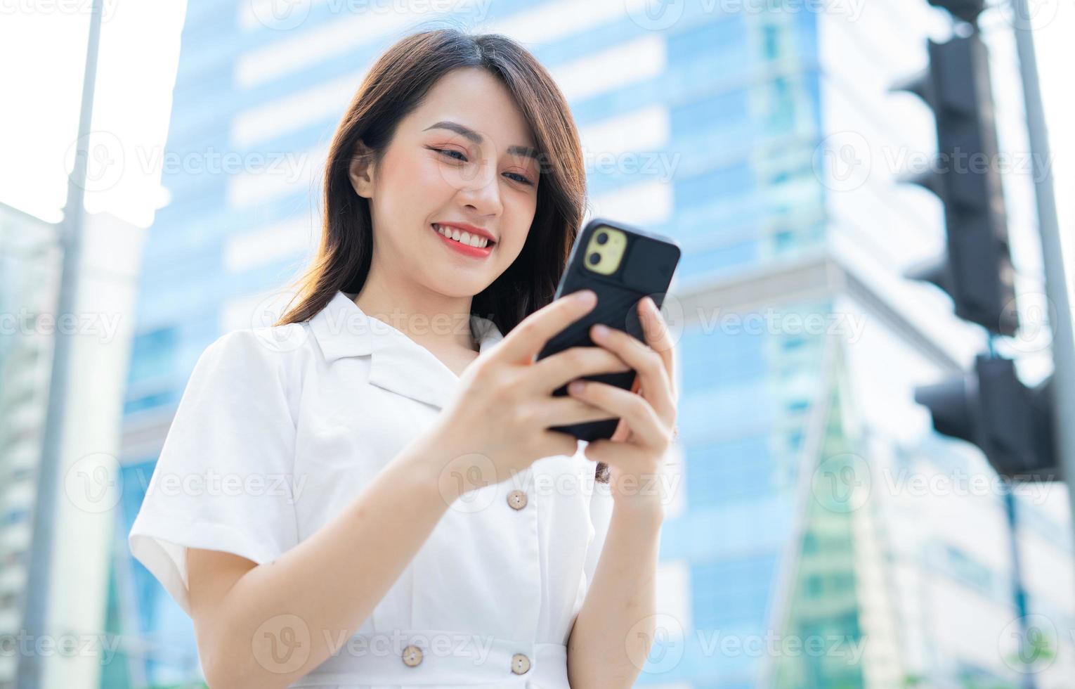 jovem mulher asiática andando e usando smartphone na rua foto