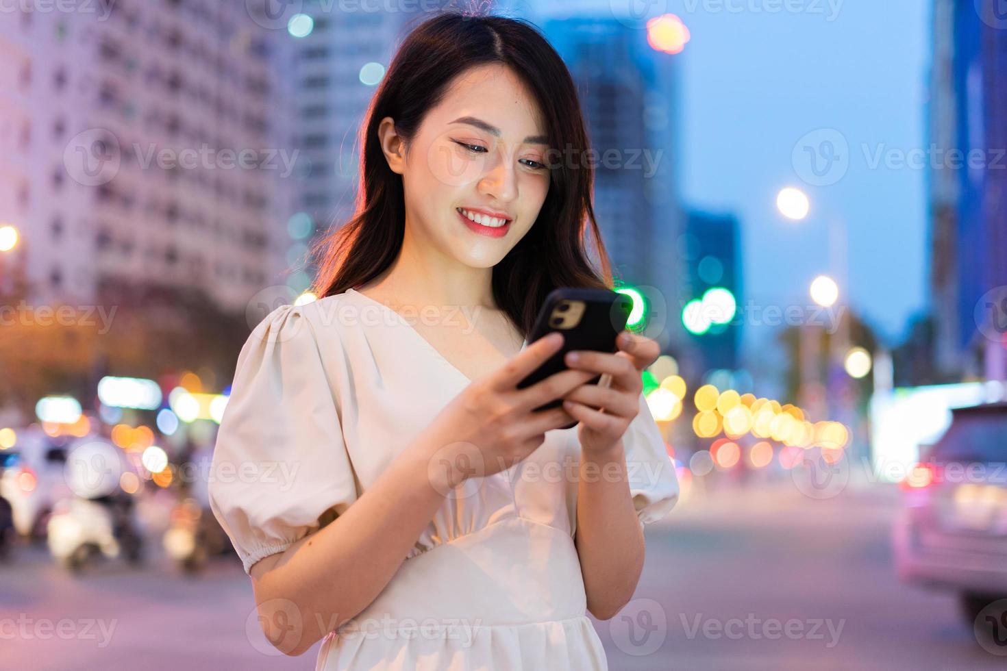 jovem mulher asiática usando smartphone na rua à noite foto