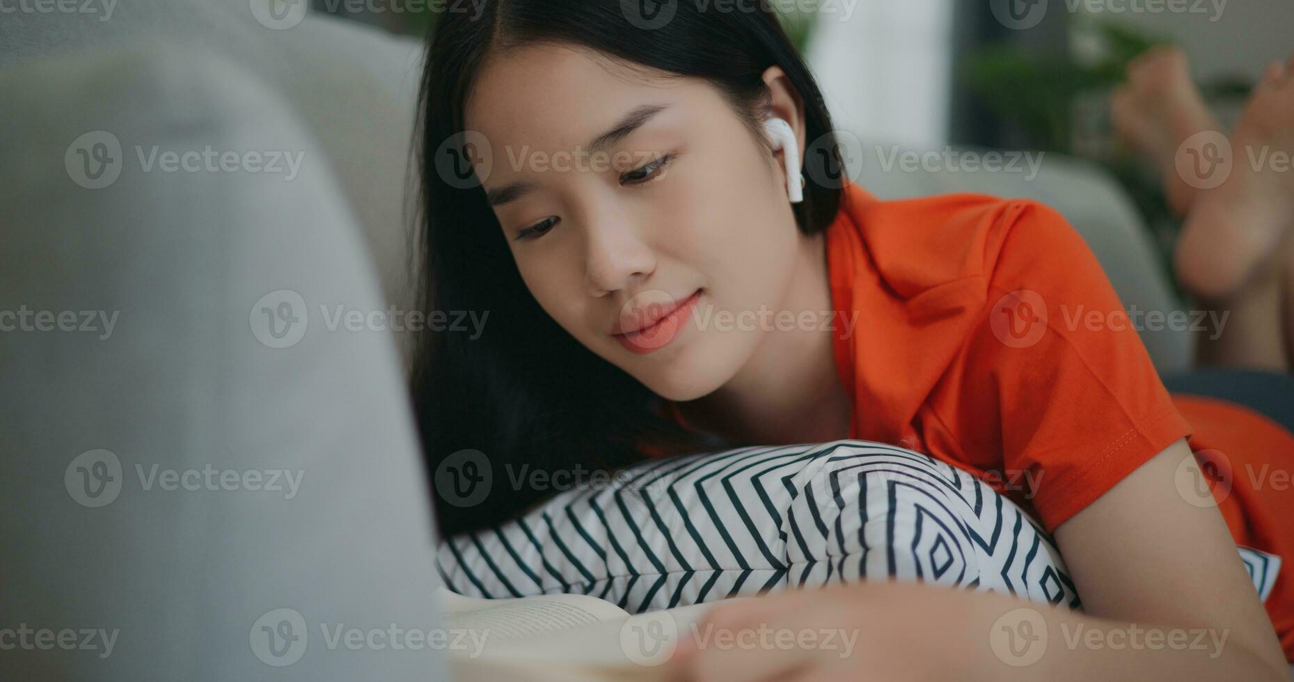 ásia mulher lendo uma livro enquanto deitado em a sofá foto