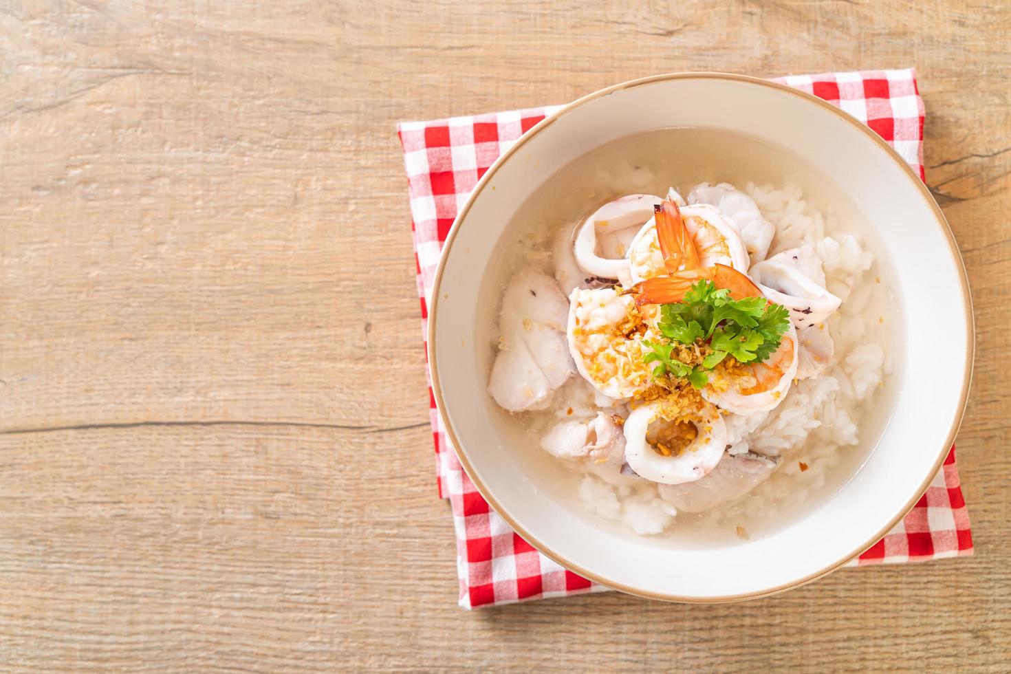 mingau ou sopa de arroz cozido com frutos do mar de camarão, lula e peixe em uma tigela foto