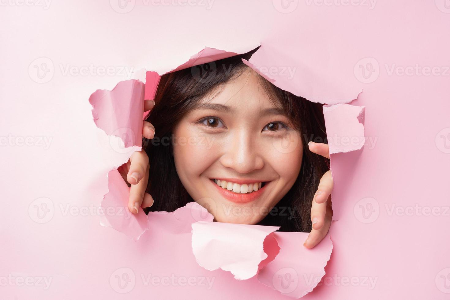jovem mulher asiática enfiou a cabeça através do papel rasgado foto