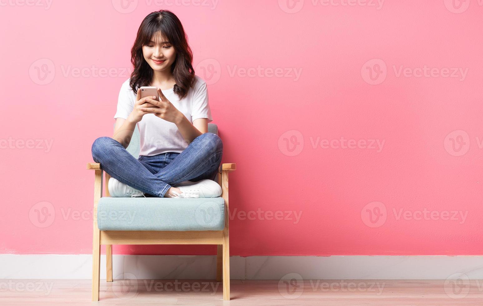 mulher asiática sentada no sofá usando o telefone com uma expressão feliz foto