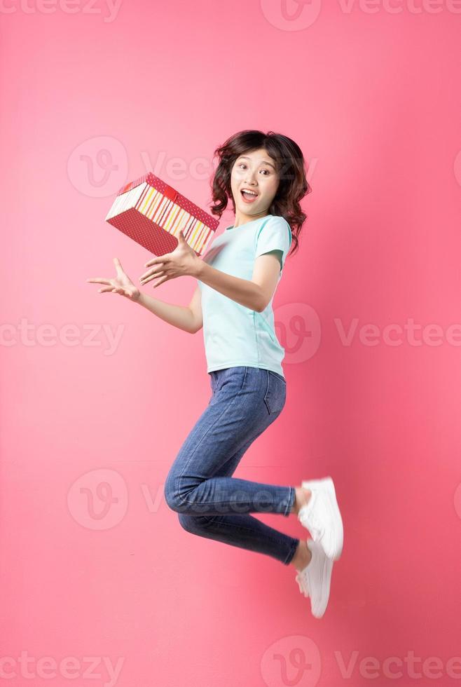 mulher segurando uma caixa de presente pulando com uma expressão alegre no fundo foto