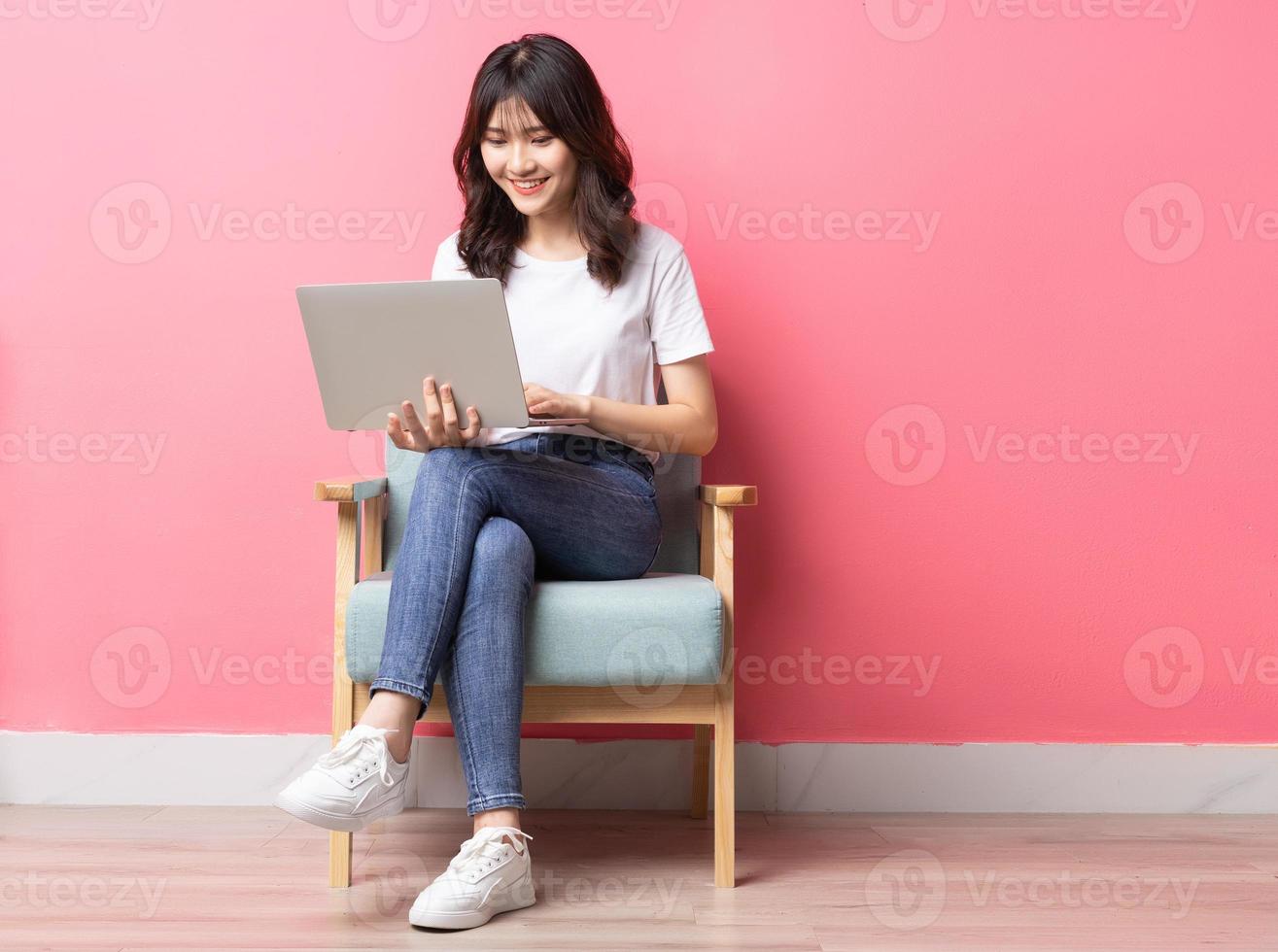 Mulher asiática sentada no sofá usando laptop com uma expressão feliz foto