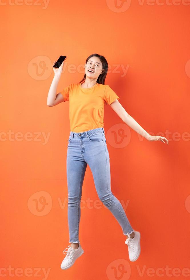jovem mulher asiática vestindo uma camiseta laranja pulando em um fundo laranja foto