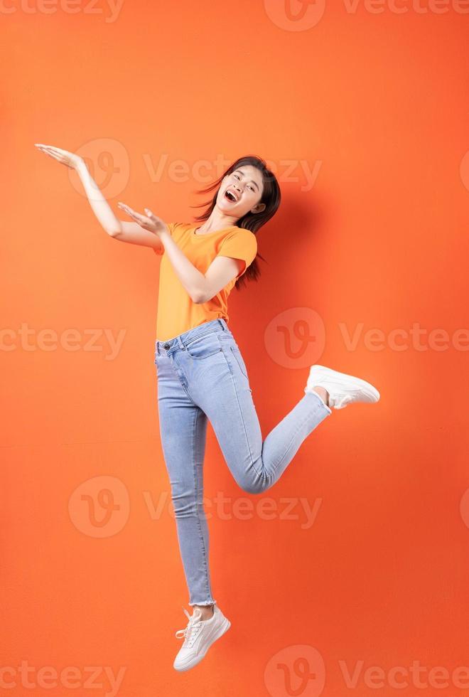jovem mulher asiática vestindo uma camiseta laranja pulando em um fundo laranja foto