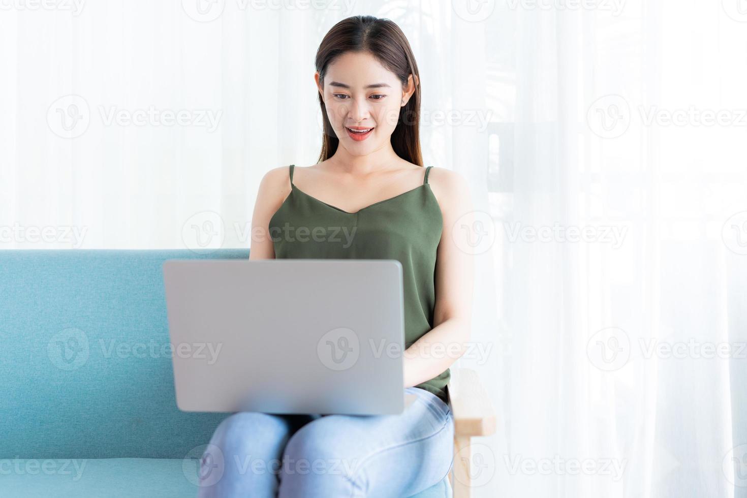 mulher asiática sentada no sofá usando um laptop foto
