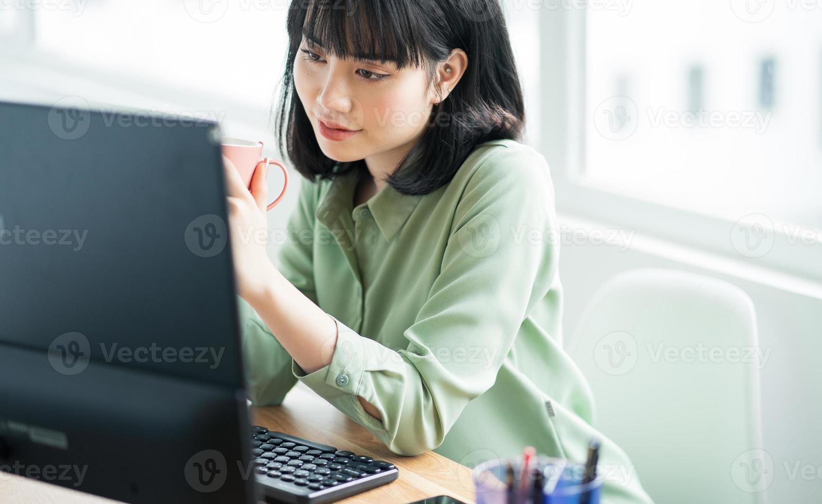 linda empresária asiática sentada e bebendo café em sua mesa durante a pausa para o almoço foto