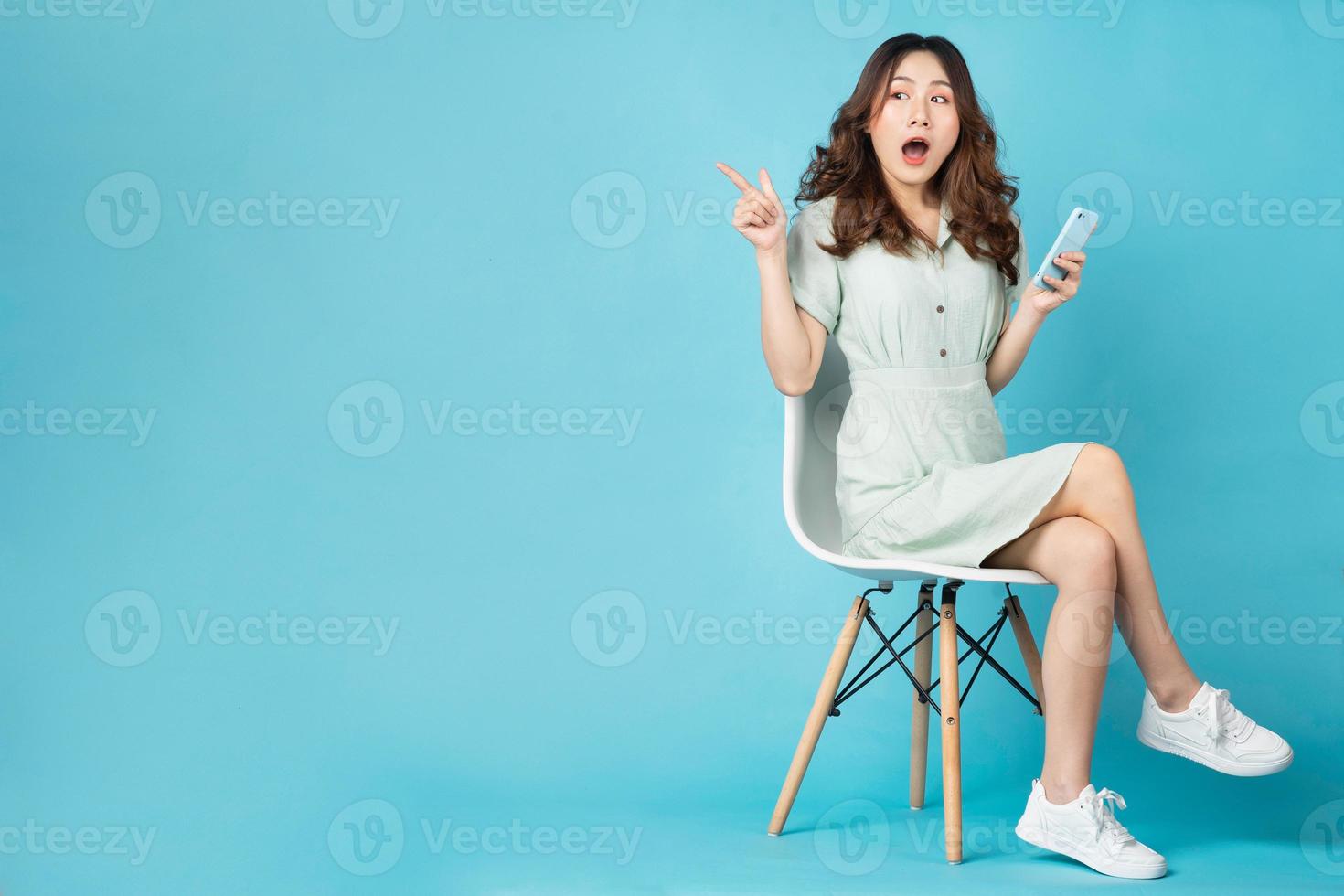 jovem asiática sentada na cadeira usando o telefone com expressão de surpresa no fundo foto
