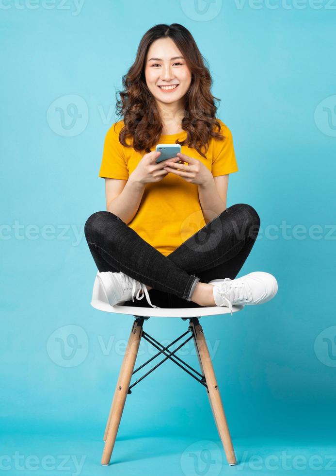 jovem asiática sentada na cadeira usando o telefone com uma expressão alegre no fundo foto