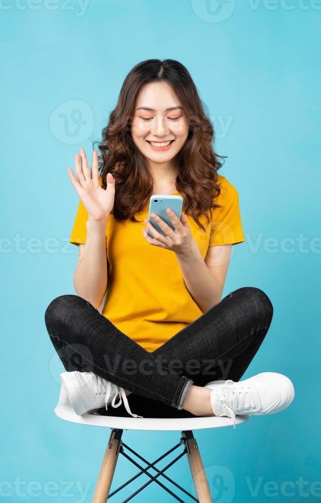 jovem asiática sentada na cadeira usando o telefone com uma expressão alegre no fundo foto