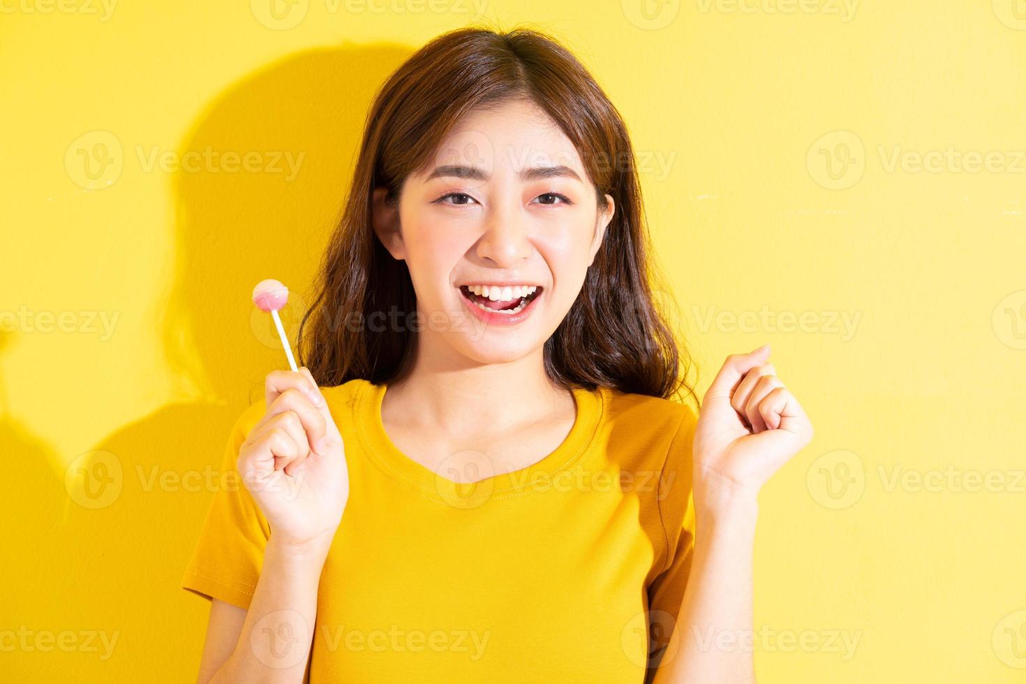 jovem mulher asiática comendo pirulito em fundo amarelo foto