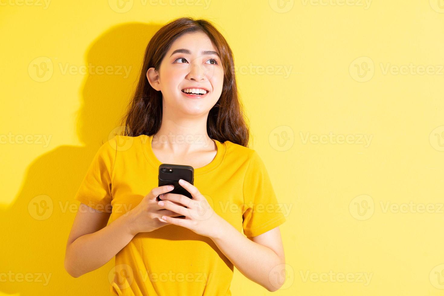 jovem asiática usando smartphone em fundo amarelo foto