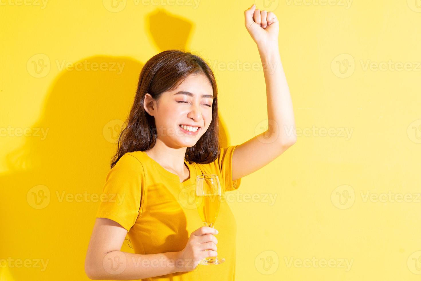 jovem mulher asiática bebendo vinho e posando em fundo amarelo foto