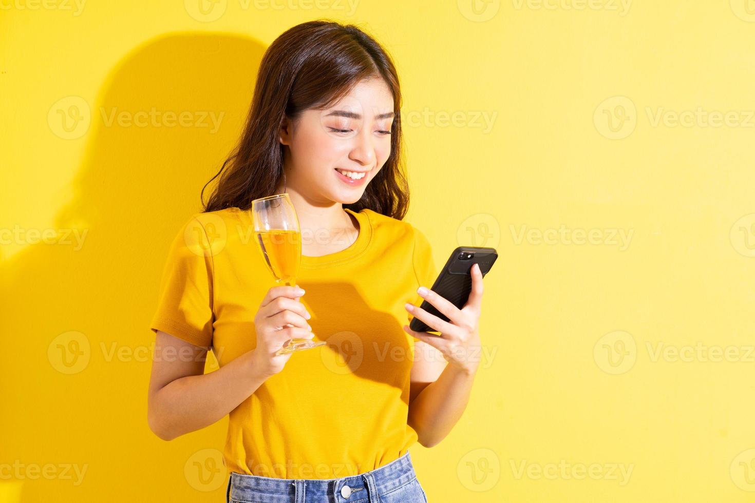 jovem mulher asiática bebendo vinho e posando em fundo amarelo foto