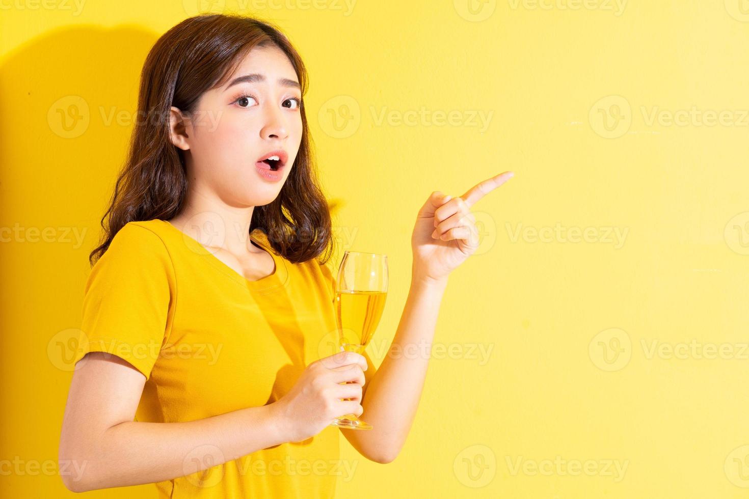 jovem mulher asiática bebendo vinho e posando em fundo amarelo foto