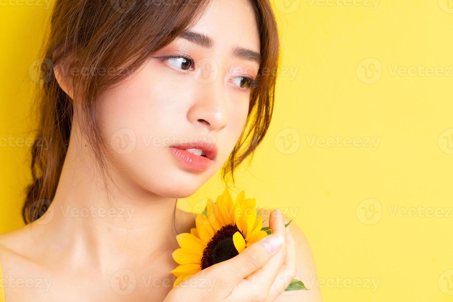 linda mulher asiática segurando e posando com girassol em fundo amarelo foto