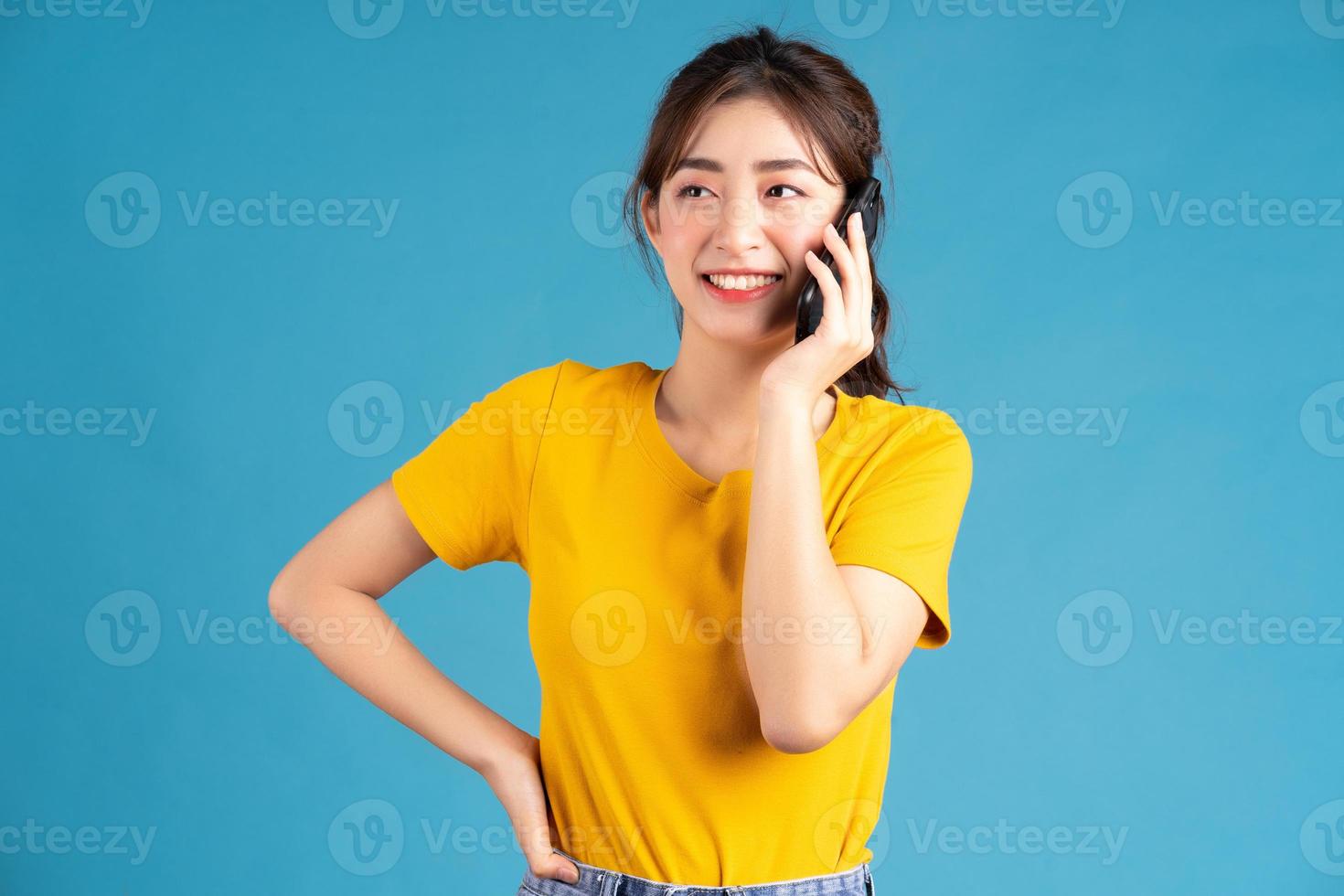 jovem mulher asiática em pé e usando o smartphone sobre fundo azul foto