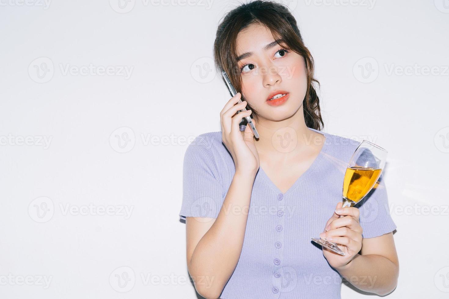 jovem mulher asiática bebendo vinho e usando o smartphone em fundo branco foto