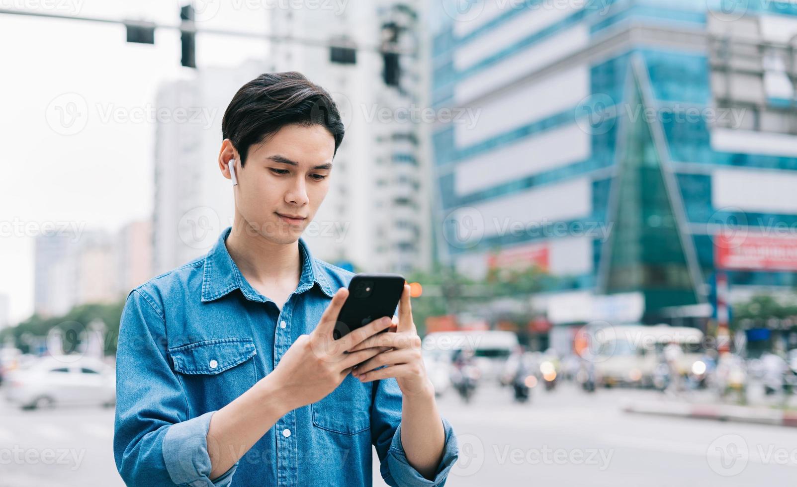 jovem asiático andando e usando smartphone na rua foto