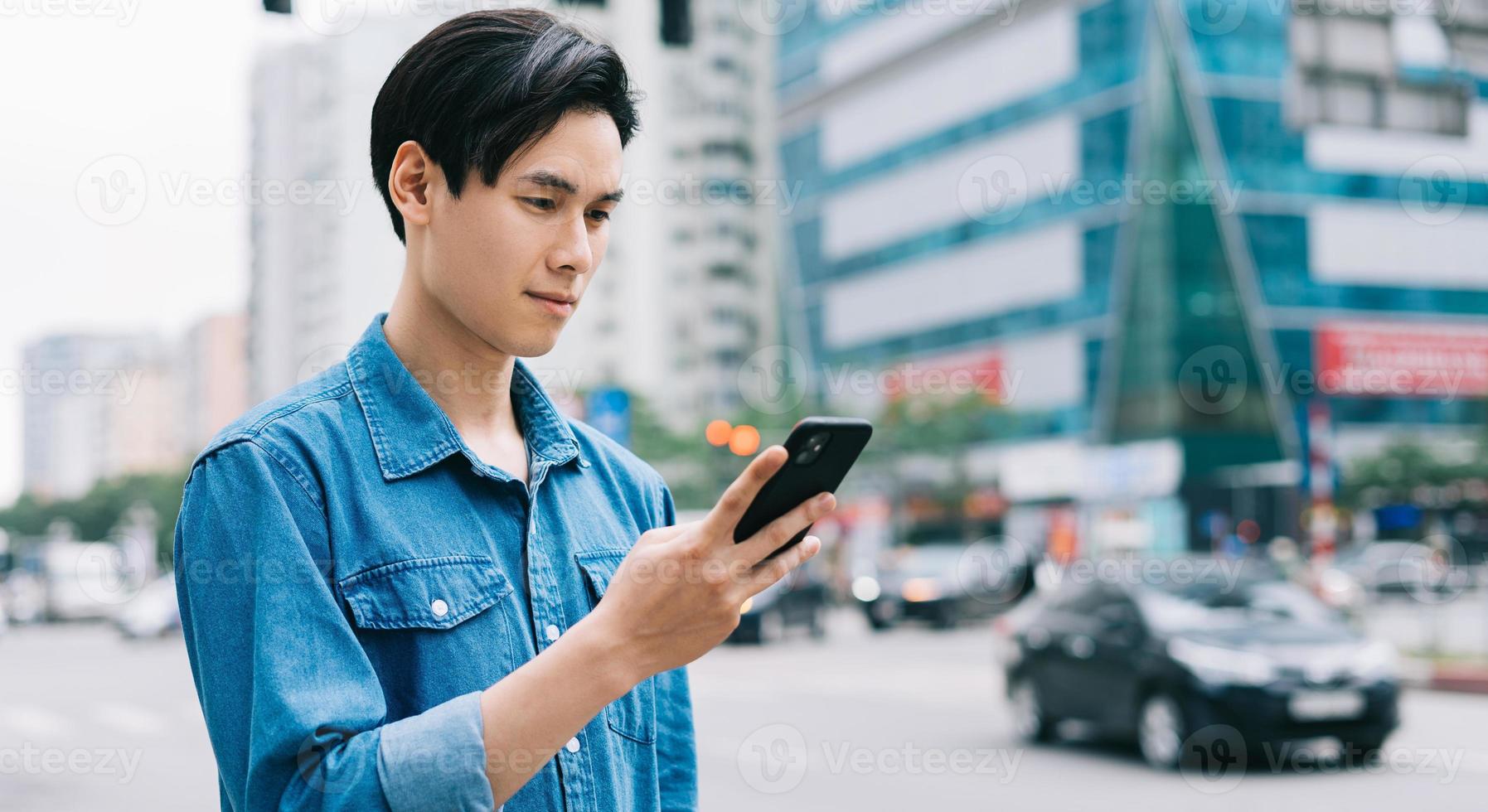 jovem asiático andando e usando smartphone na rua foto