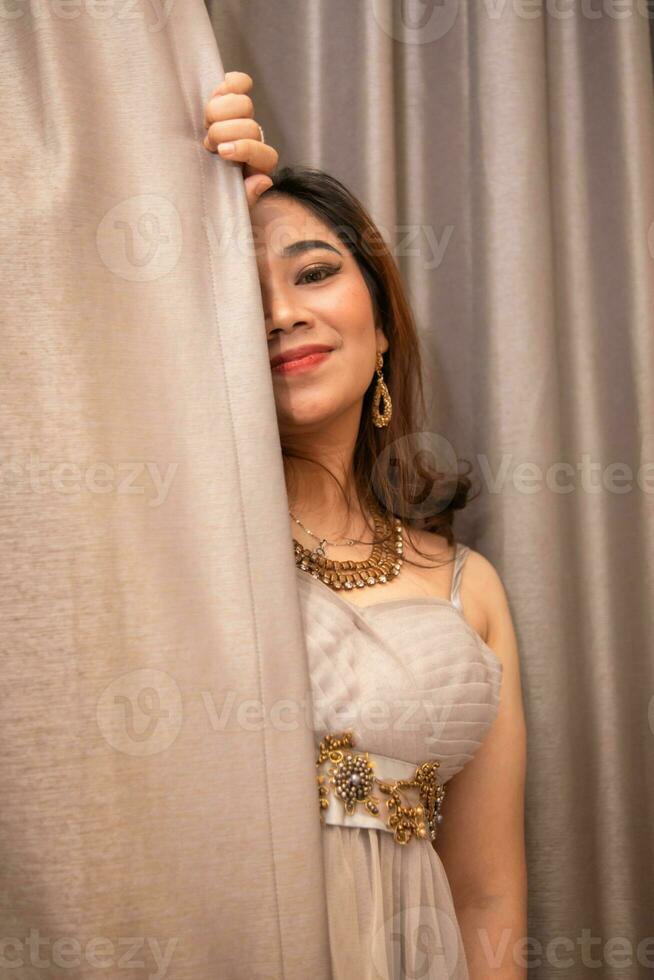 uma lindo ásia mulher segurando a cortinas enquanto posando para fotos dentro uma estúdio