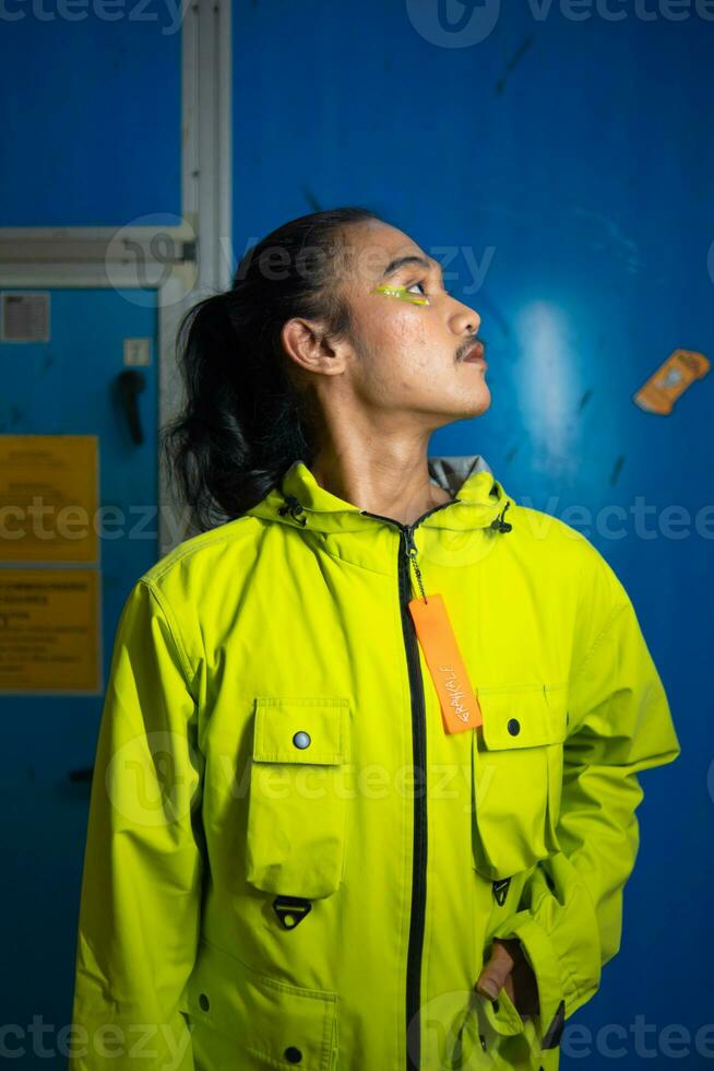 a ásia homem dentro uma verde Jaqueta é posando dentro frente do uma azul porta foto