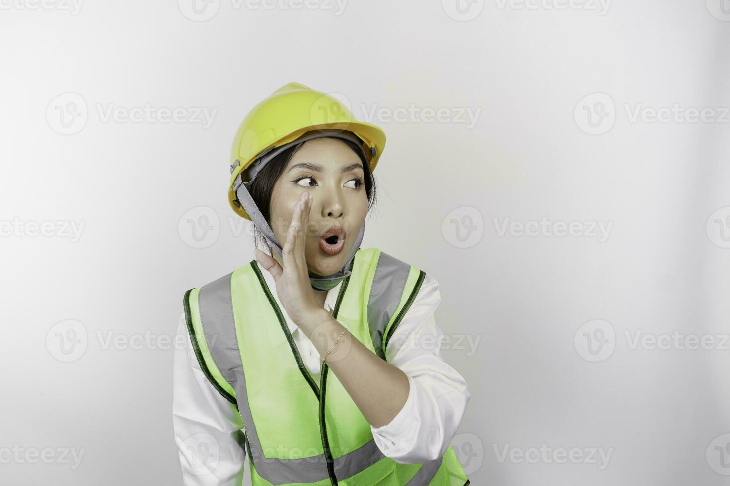 jovem lindo mulher trabalho vestindo segurança capacete e colete é gritando e gritando alto com uma mão em dela boca. trabalho dia conceito. foto