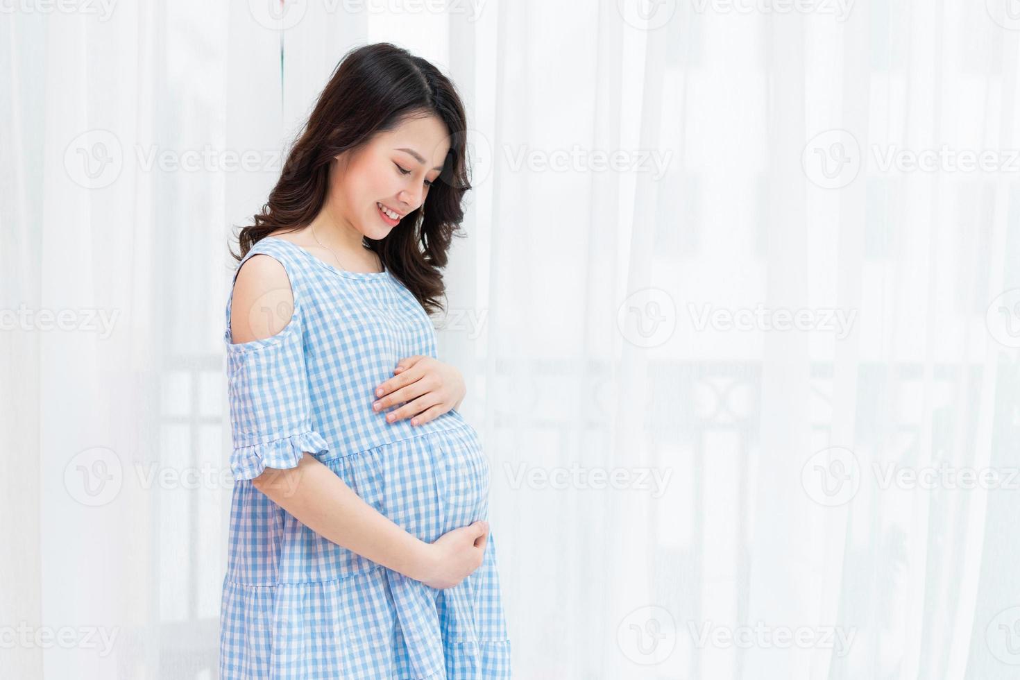 linda mulher segurando a barriga grávida perto da janela foto