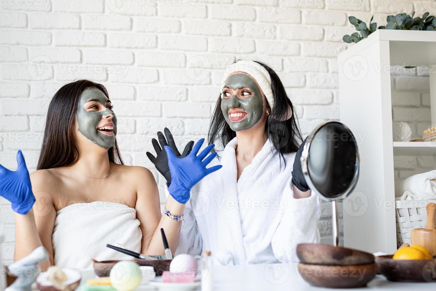 duas lindas mulheres em luvas aplicando máscara facial se divertindo foto