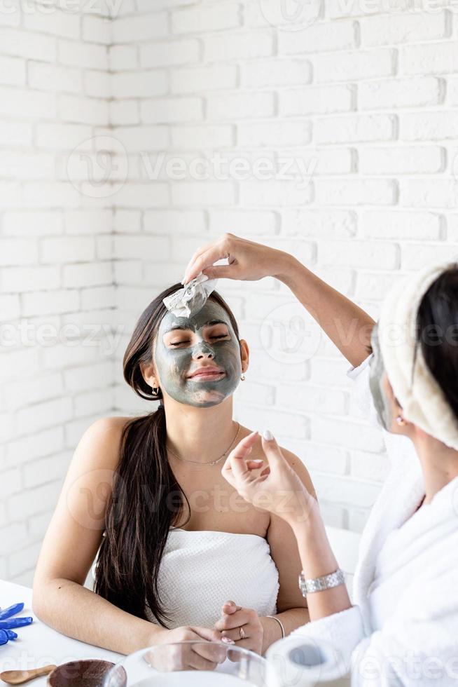 duas lindas mulheres aplicando máscara facial fazendo procedimentos de spa foto