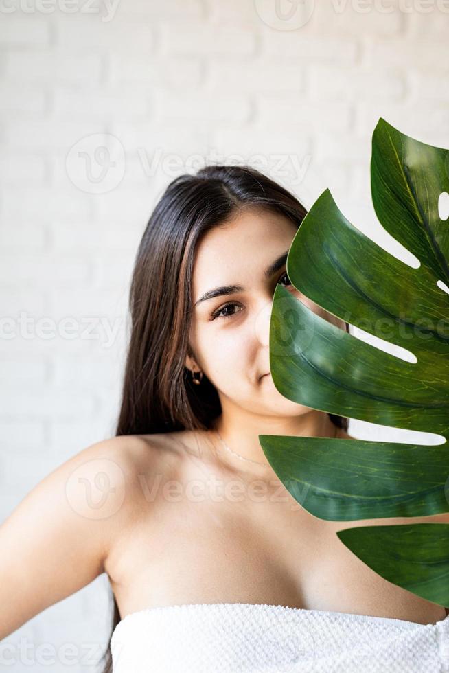 Mulher bonita e feliz usando toalhas de banho, segurando uma folha de monstro verde na frente do rosto foto