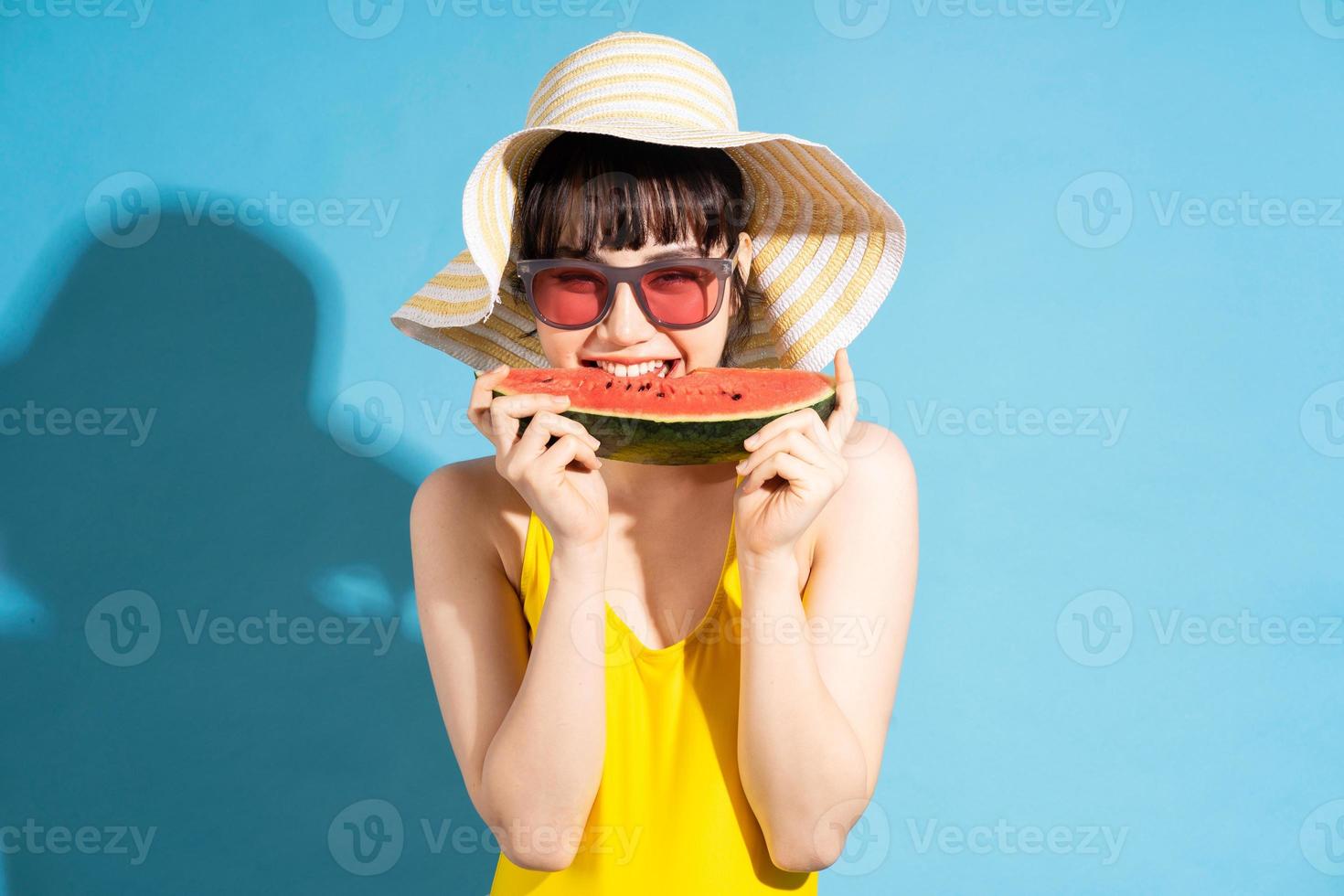 linda mulher asiática vestindo macacão amarelo sobre fundo azul e comendo frutas tropicais, conceito de verão foto