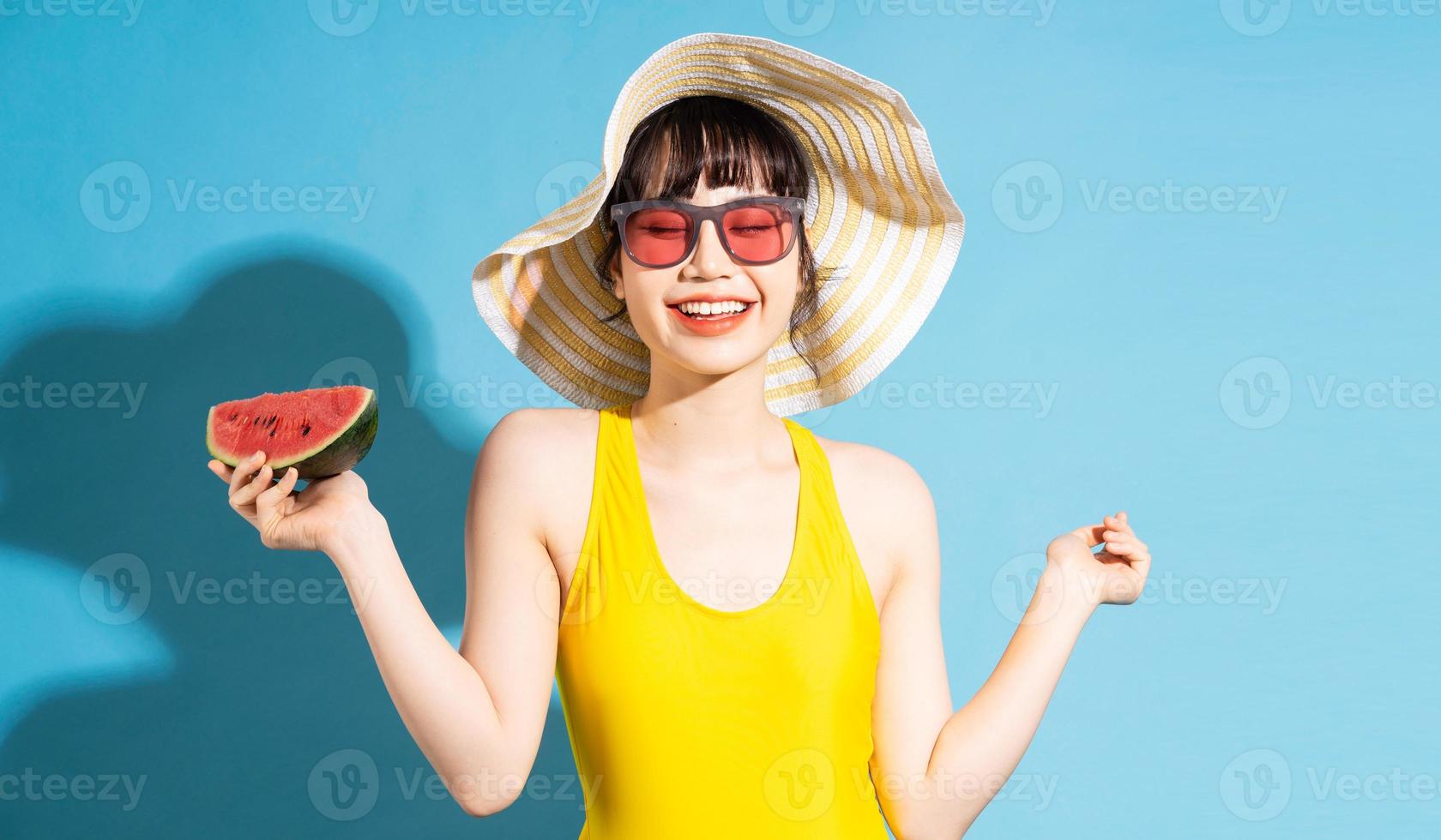 linda mulher asiática vestindo macacão amarelo sobre fundo azul e comendo frutas tropicais, conceito de verão foto