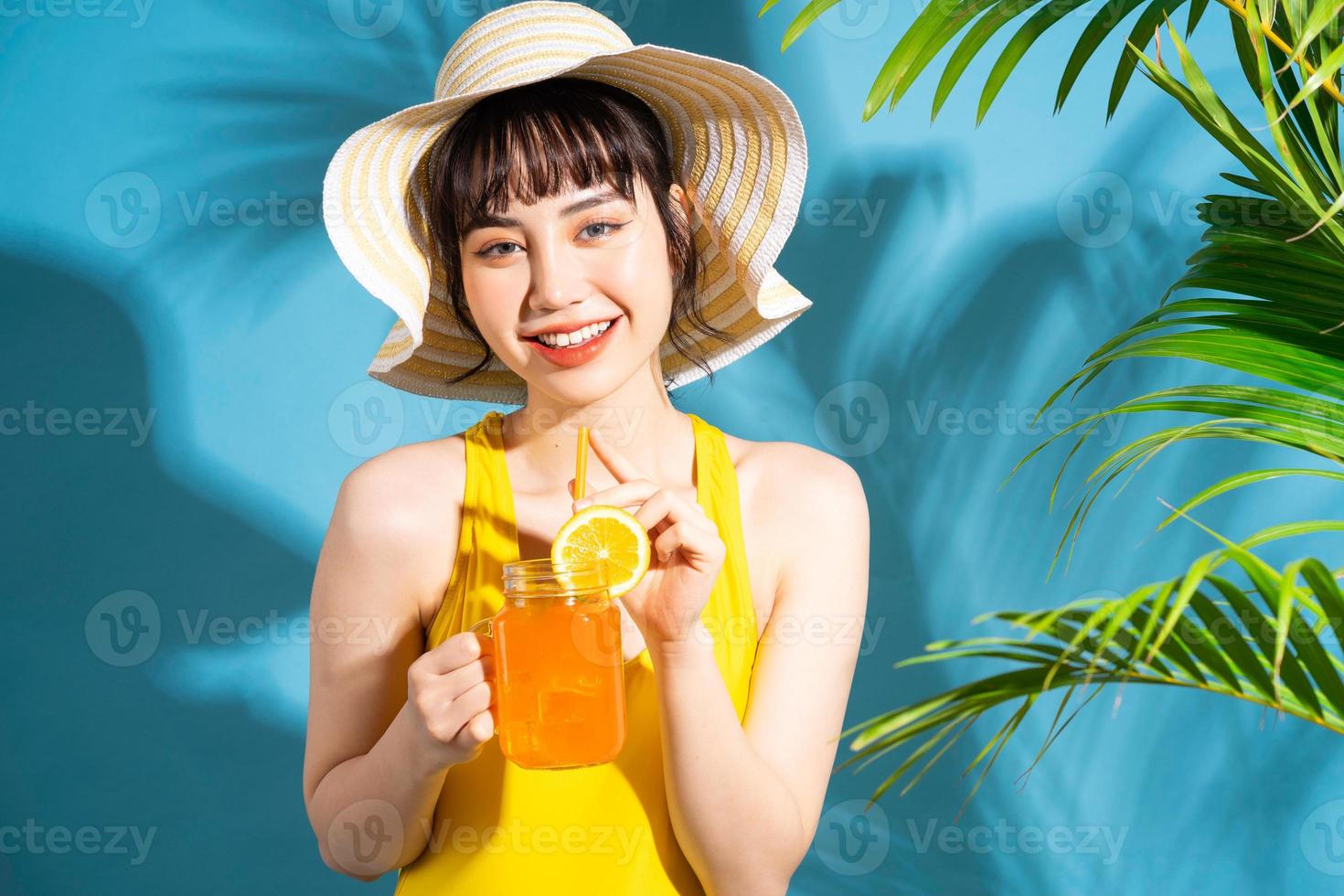 linda mulher asiática vestindo macacão amarelo sobre fundo azul e bebendo suco, conceito de verão foto